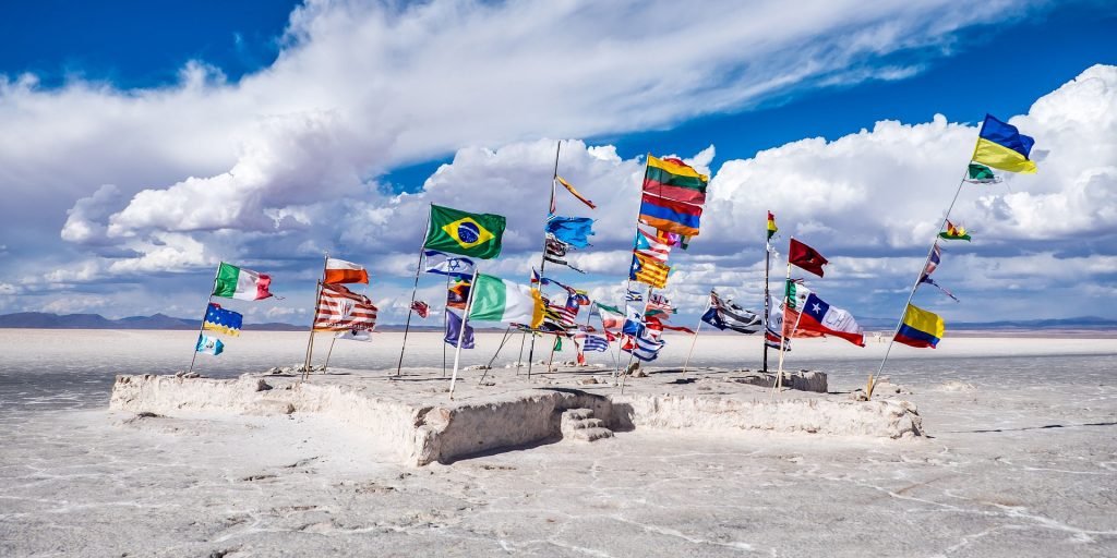 Selection of world flags flap in the wind on the beach against a blue sky