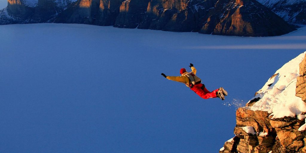 person base jumping off a cliff against a snowy mountain backdrop